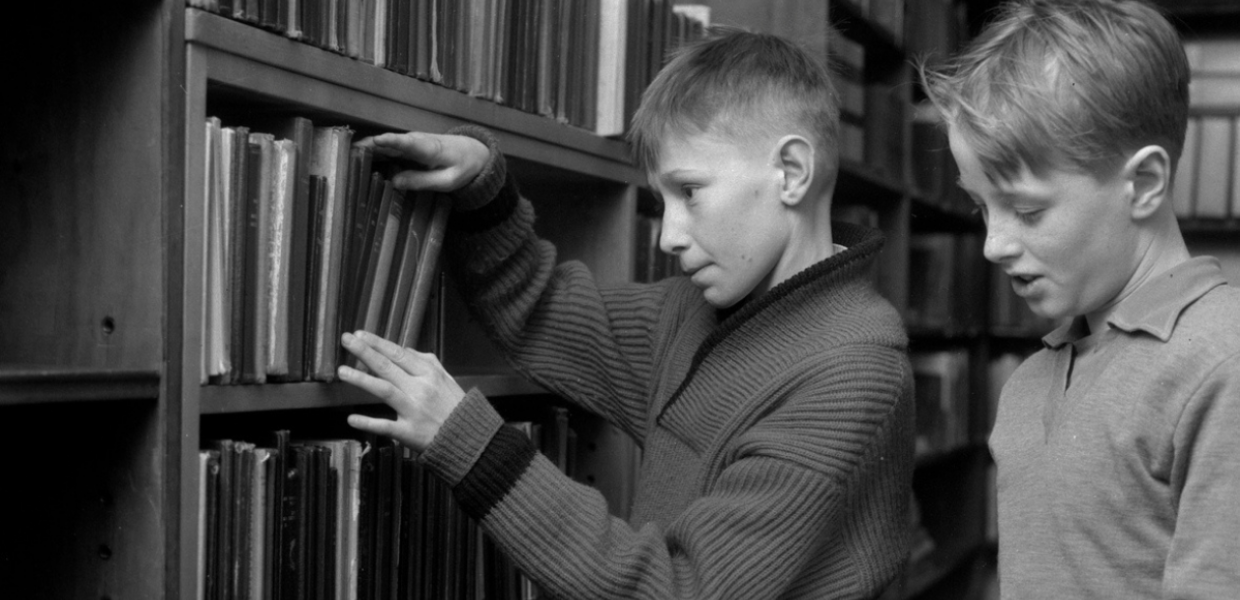 Two young boys look at books on a bookshelf